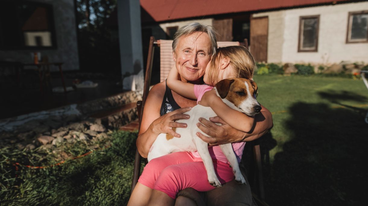 grandmother sitting in chair outside with grandaughter and dog on her lap