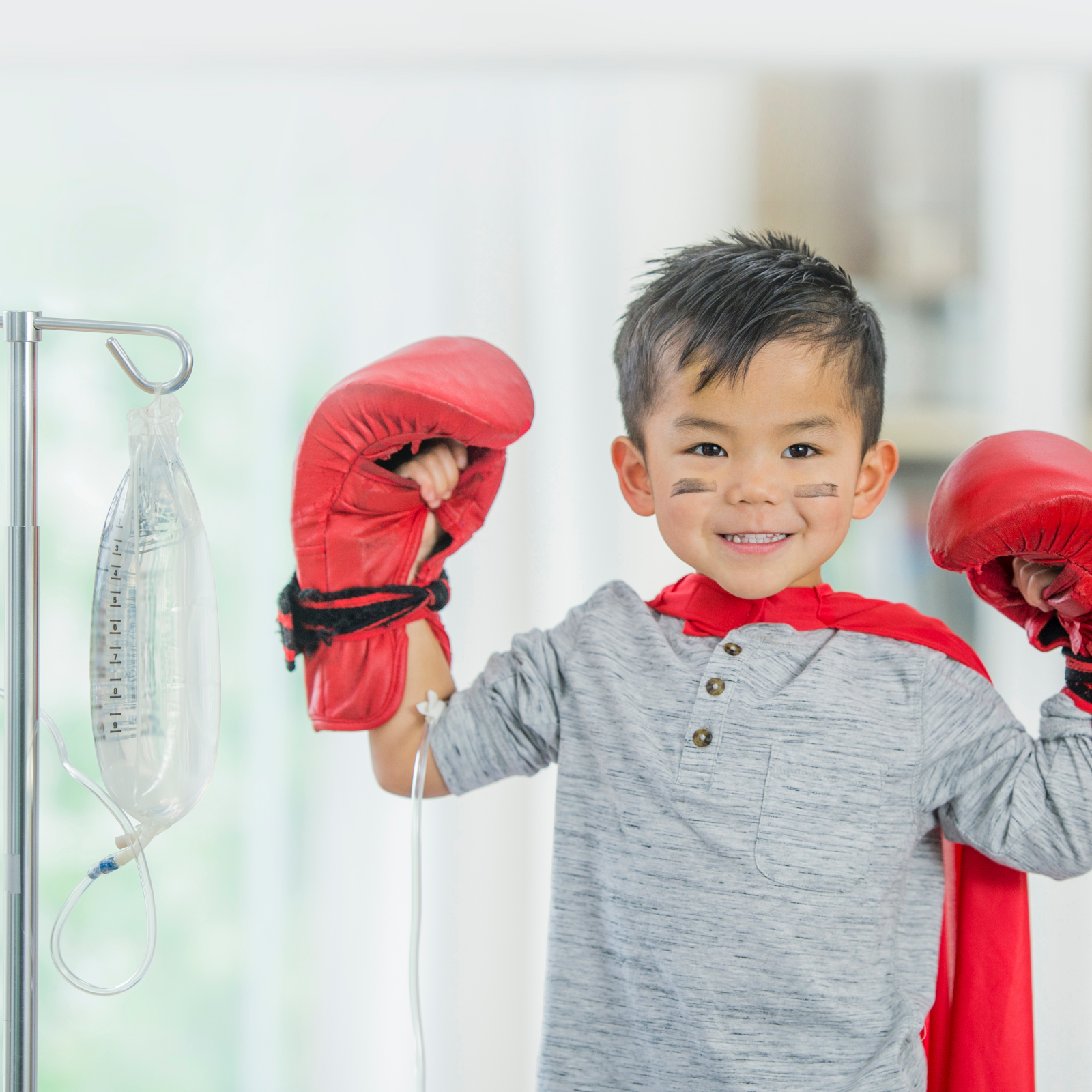 Little boy getting iv treatment wearing cape and boxing gloves