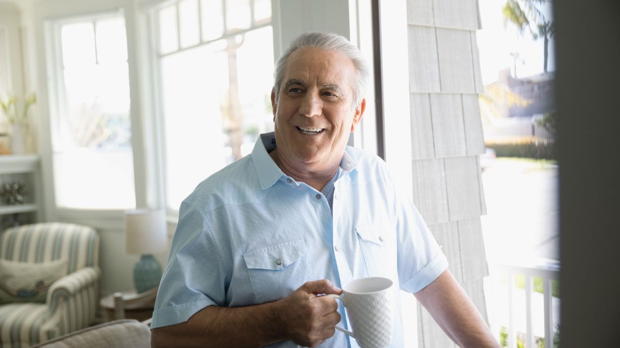 man holding coffee cup standing by door smiling