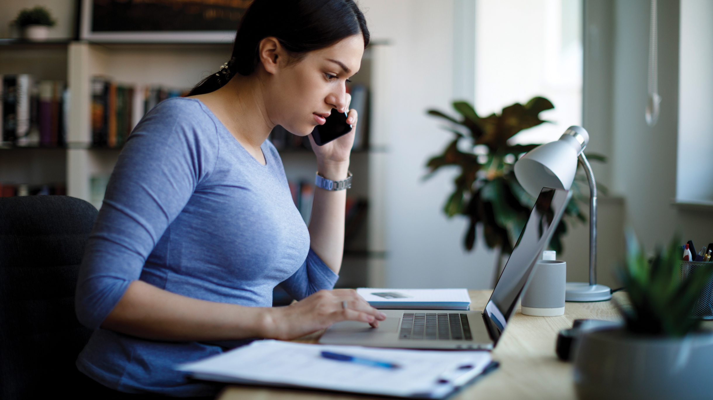 woman on her phone in front of laptop at home desk